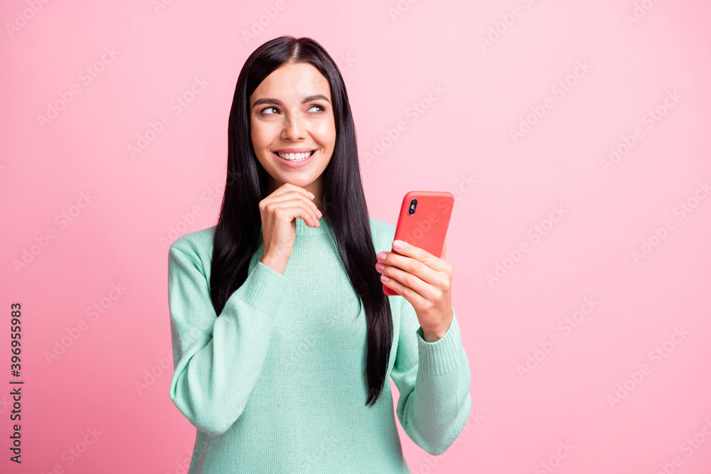 Photo portrait of minded woman touching face chin holding phone in one hand isolated on pastel pink colored background Photo portrait of minded woman touching face chin holding phone in one hand isolated on pastel pink colored background
