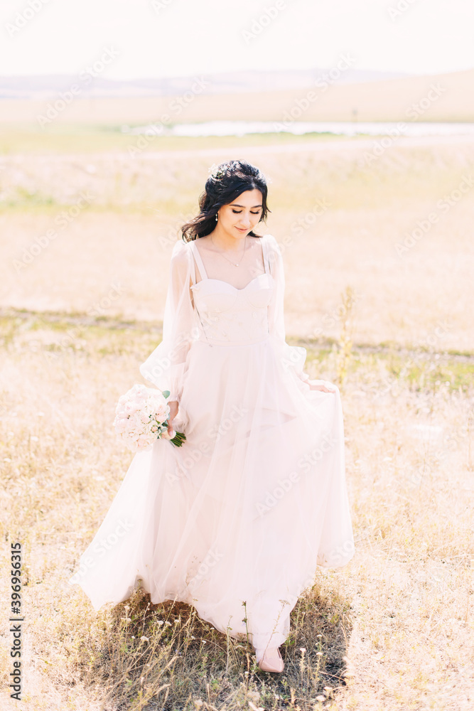 The bride walks in a powdery dress with a wedding bouquet in her hands on the background of nature