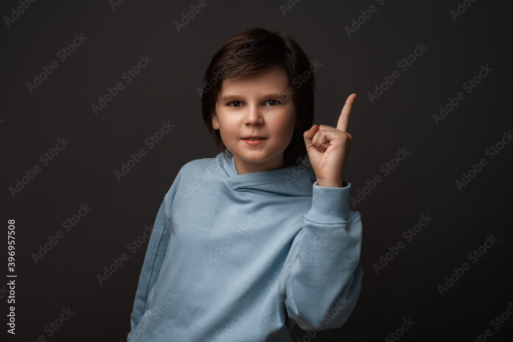 Portrait of Serious boy showing index finger. Studio shot, gray background. Human emotions, facial expression concept Portrait of Serious boy showing index finger. Studio shot, gray background. Human emotions, facial expression concept