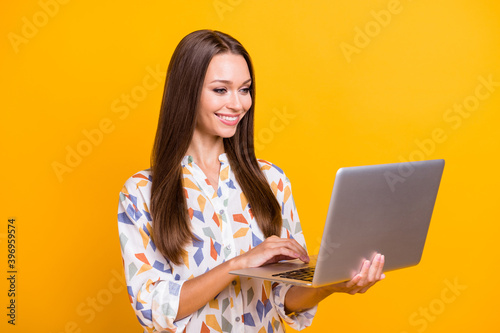 Photo portrait of girl holding laptop typing isolated on vivid yellow colored background