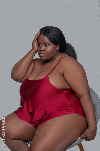 Plus size african american young woman in red underwear sitting on a chair and looking upset