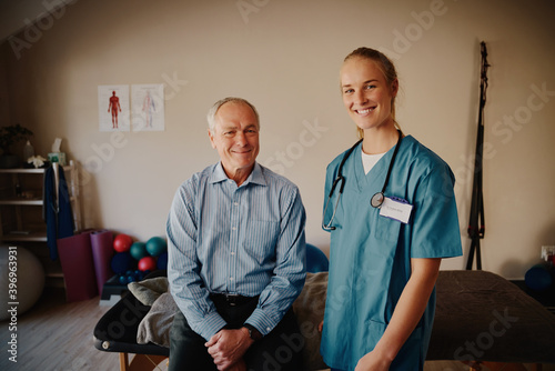 Portrait of smiling senior man with young doctor in uniform and stethoscope looking at camera