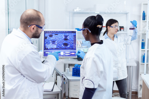 African doctor and scientist working conducting virus experiment using computer software. Multiethnic team of medical researchers working together in sterile lab wearing protection glasses and gloves.