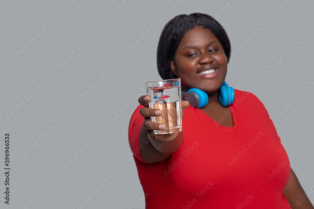 Young dark-skinned woman with headphones holding a glass of water Young dark-skinned woman with headphones holding a glass of water