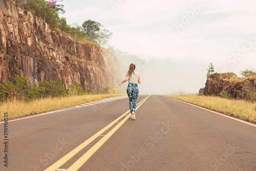 Fototapeta Naklejka Na Ścianę i Meble -  Full image of a young athlete running outdoors on an open road in the countryside - Dedicated female athlete running backwards.