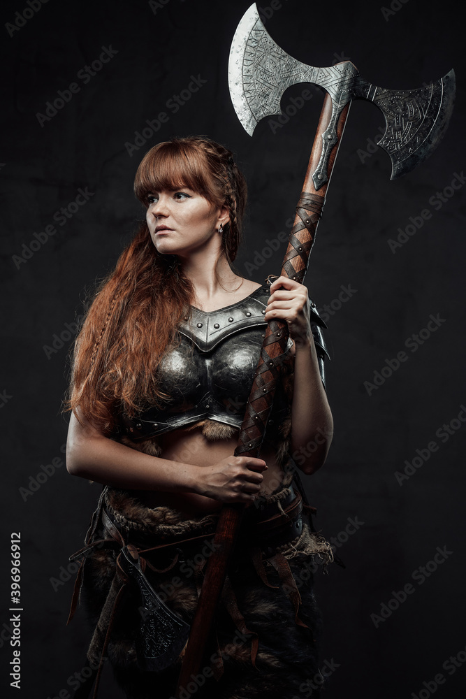 Armed With Huge Axe And Armoured Woman Viking With Long Brown Hairs Poses In Dark Background