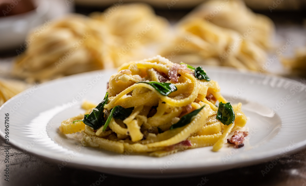 Cooked fresh fettuccine pasta served on a plate with spinach and bacon