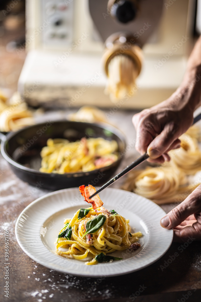 Hands of chef plating freshly cooked pasta with a pasta maker in the background Hands of chef plating freshly cooked pasta with a pasta maker in the background