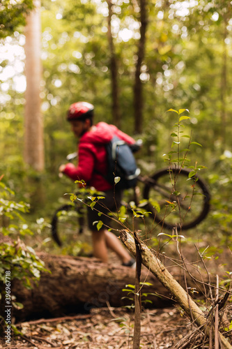 A young professional cyclist in sportswear wearing a helmet outdoors - Young male cyclist carrying his mountain bike in the jungle.