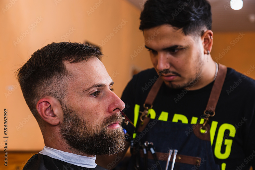 Fototapeta premium The barber does the haircut for the client in the barber's shop - Men's haircut with electric shaver.