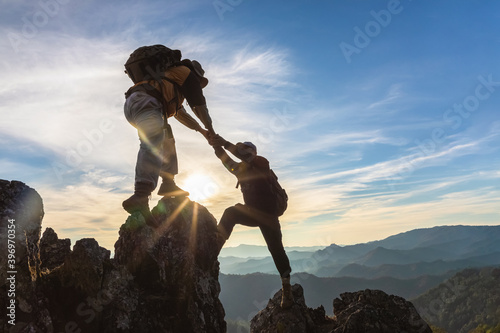 Silhouette Two Male hikers climbing up mountain cliff and one of them giving helping hand. People helping and, team work concept. photo