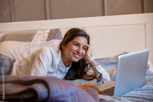 Portrait of a smiling businesswoman typing on her laptop in bed after the workday.