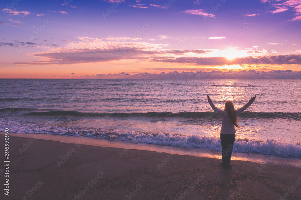 Seascape at sunrise with beautiful sky. Woman on the beach during sunrise. Young happy woman with hands in the air stands on the beach and gazes at sunrise