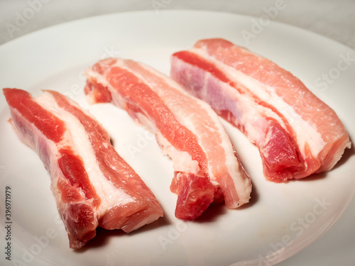 Fresh raw pork belly slices on a white plate. Meat industry product