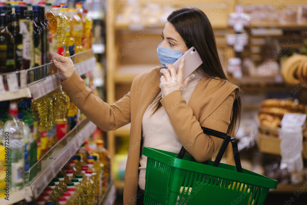 Buyer wearing a protective mask and gloves in supermarket. Shopping during the pandemic quarantine Covid-19. Nonperishable smart purchased household pantry groceries preparation. Woman spear by phone
