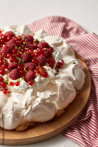 food, culinary, baking and cooking concept - close up of pavlova meringue cake decorated with red berries on wooden serving board and kitchen towel
