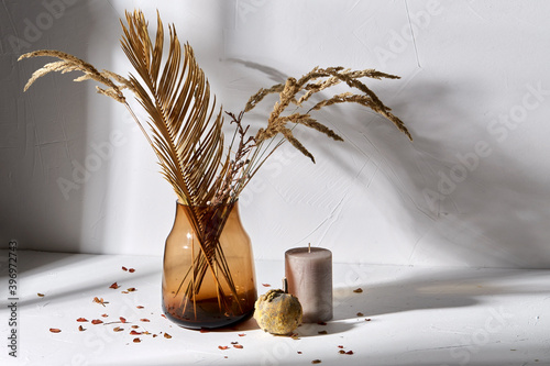 Fototapeta Naklejka Na Ścianę i Meble -  home improvement and decoration concept - still life of decorative dried flowers in brown glass vase, candle and pumpkin
