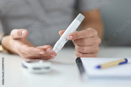 Woman holding lancet near her finger to measure blood glucose closeup