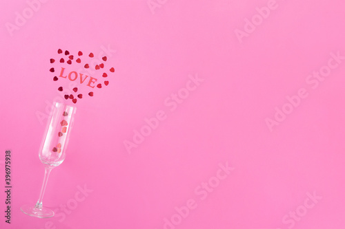 Glass of champagne with red hearts and word love on a pink background. Valentines background, love, date concept with copy space, flatlay