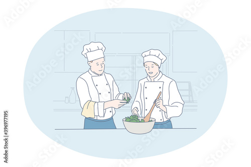 Cooking, professional chef, restaurant concept. Young man and woman professional cooks in aprons and hats cooking healthy salad or dish together in kitchen of cafe Gourmet, delicious, tasty menu 