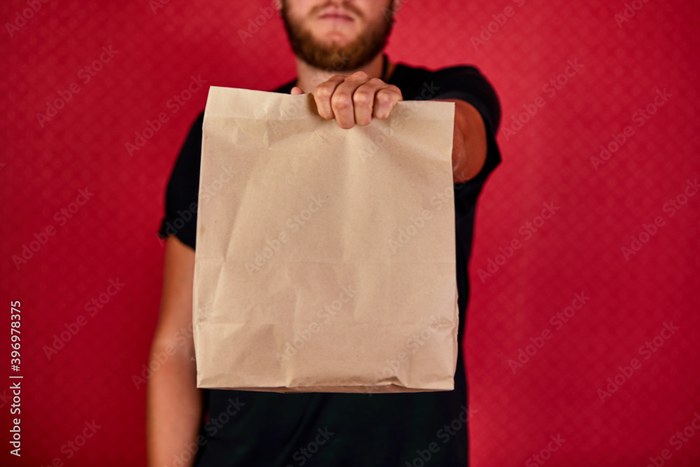 Courier, delivery man in black uniform delivers online purchases in brown paper bags