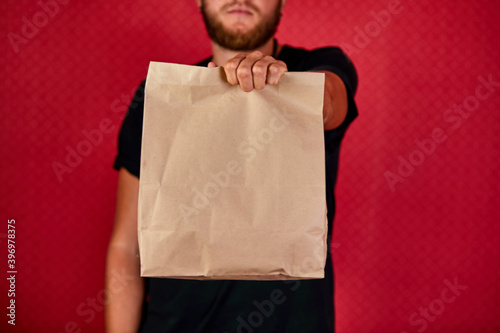 Courier, delivery man in black uniform delivers online purchases in brown paper bags