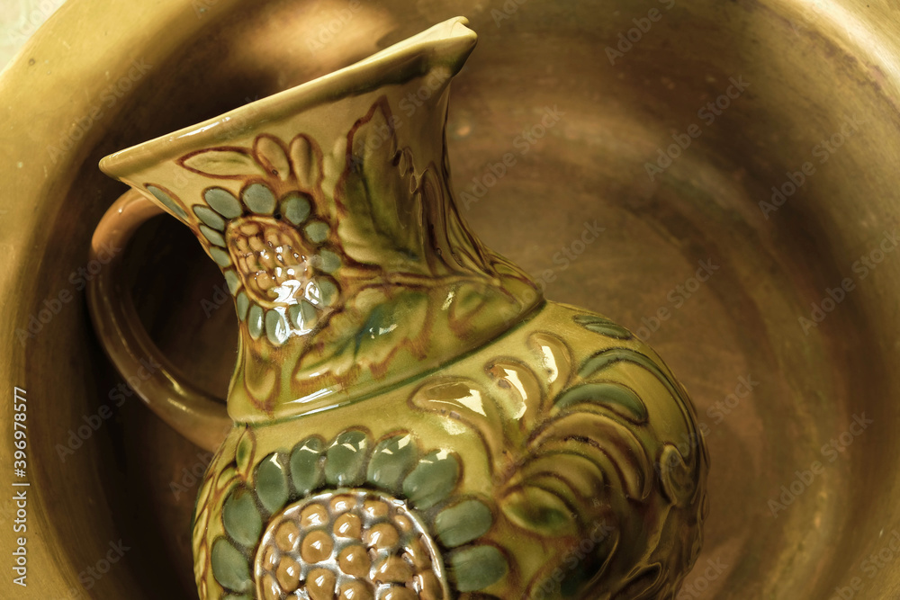 A traditional former Ukrainian ceramic jug with sunflowers lies in a copper bowl. Monochrome image. Ukrainian culture concept. Mass-produced jug. Copy space.