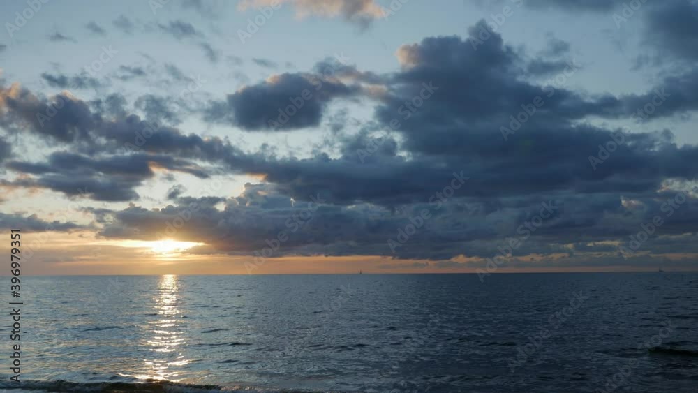 Sunset at sea with a blue cloudy sky and two sailboats on the horizon. Handheld shot. Sunset at sea with a blue cloudy sky and two sailboats on the horizon. Handheld shot.