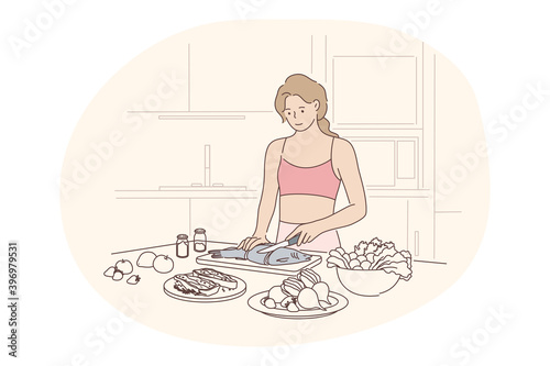 Healthy homemade food, clean eating, diet concept. Young positive woman standing in kitchen and cooking fish with fresh vegetables for dinner at home alone. Wellness, bodycare, healthy lifestyle