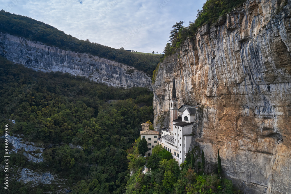 The unique Sanctuary Madonna della Corona church in the rock. The sanctuary is high in the mountains of Italy. Aerial view of the church on the sheer cliff. Italian church at high altitude in the Alps