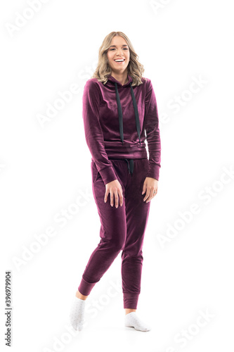 Cheerful candid young beautiful woman in burgundy sweatsuit and socks laughing hard hearing jokes. Full body length isolated on white background. 