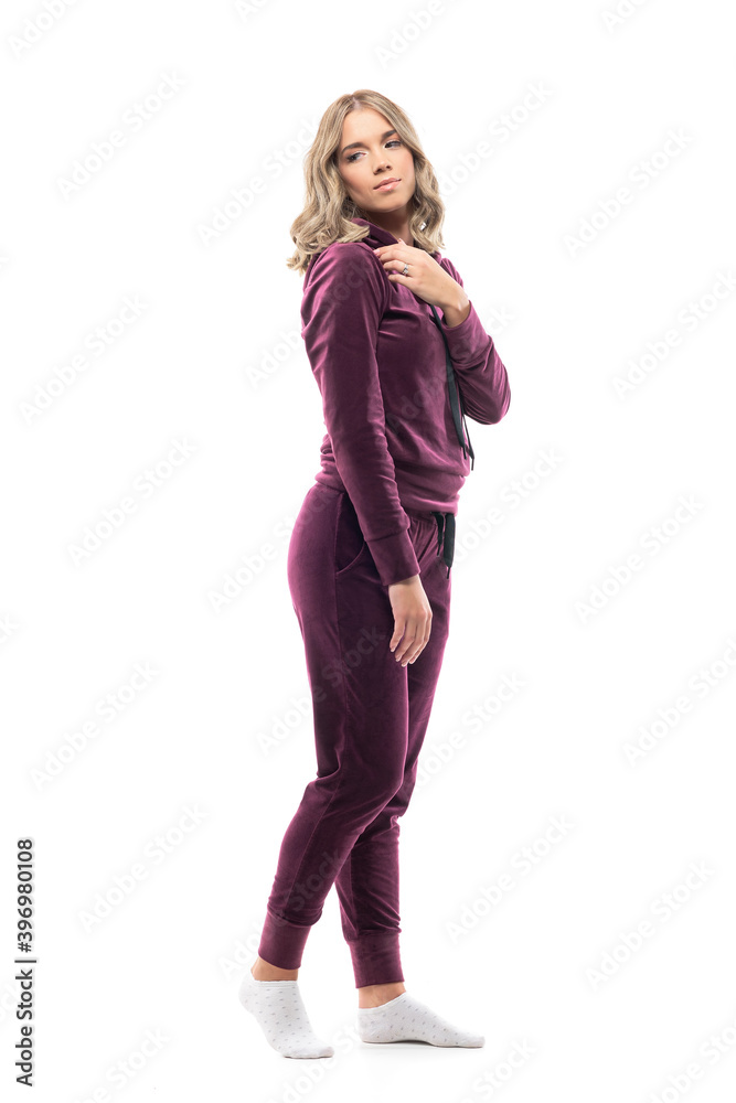 Fototapeta premium Side view of cute feminine young beauty woman in comfy sweatsuit looking back touching shoulder. Full body length isolated on white background. 