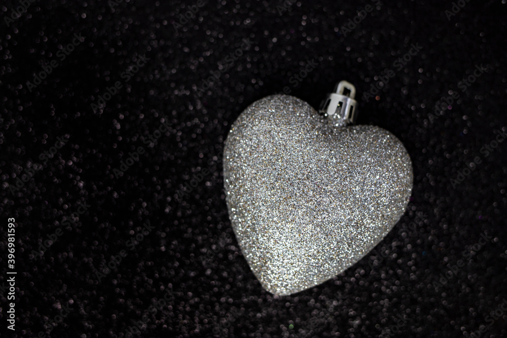 Christmas tree toy in the form of a heart of silver on a shiny black background. Flat lay, place for text. Christmas tree toy in the form of a heart of silver on a shiny black background. Flat lay, place for text.