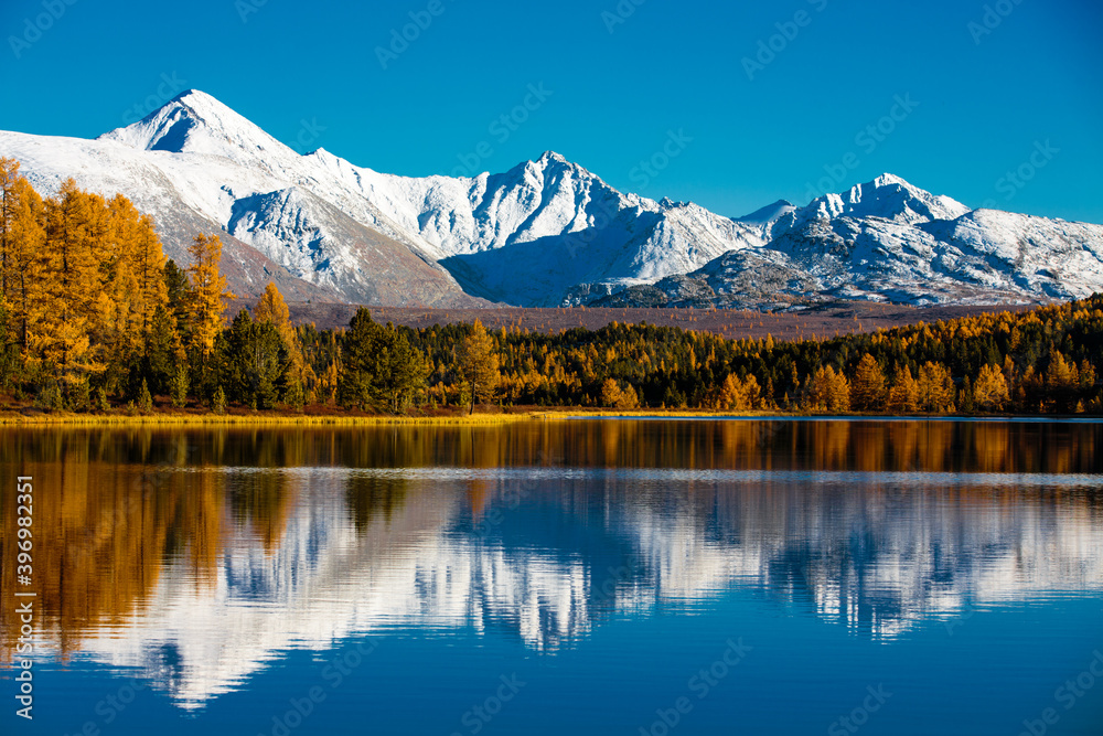 Mountain lake on a background of snow-white mountains and golden autumn nature. Mountains are reflected in the water.