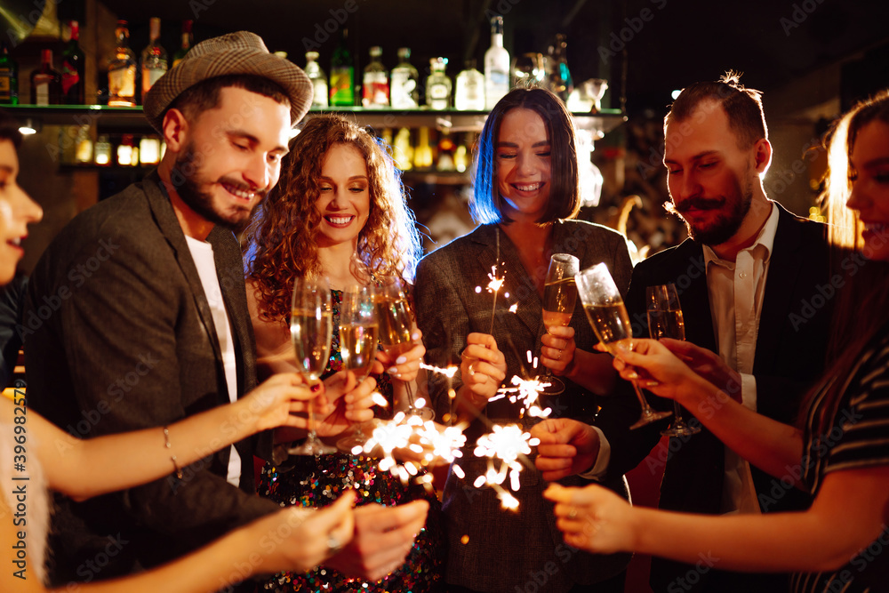 Friends celebrate Christmas or New Years party with sparklers and champagne. Group of happy people enjoying party with fireworks.Winter holiday, youth, lifestyle concept.