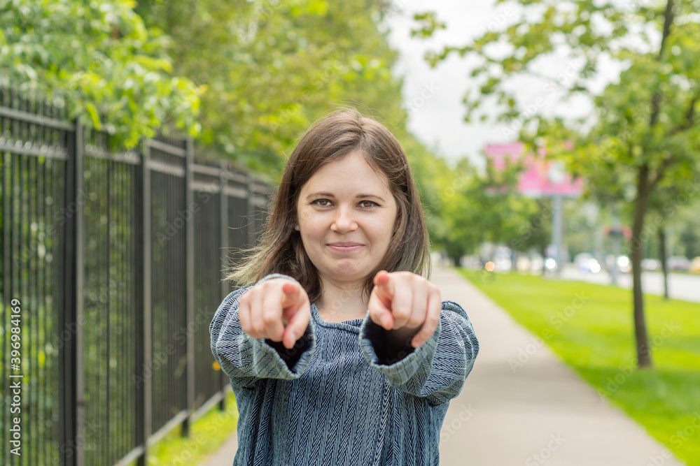 Smiling girl shows a finger forward while standing on the street against the background of the road and park. The concept is a call to move forward or we need you. Smiling girl shows a finger forward while standing on the street against the background of the road and park. The concept is a call to move forward or we need you.