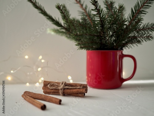 Christmas red enamel Cup, fir branches, cinnamon sticks on a background, lights garlands