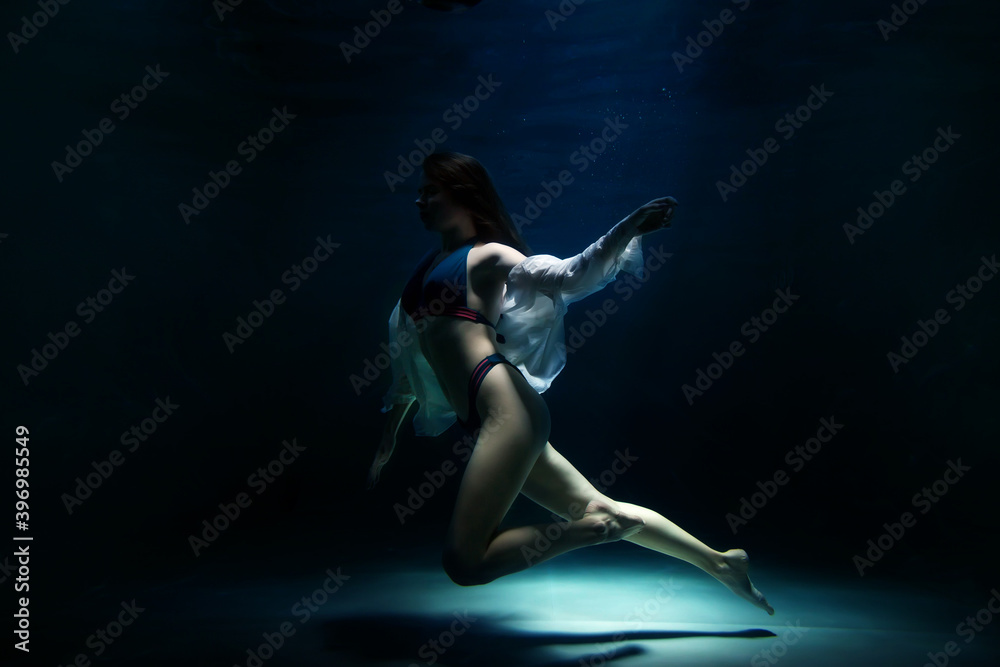 Slender pretty young woman brunette in bathing suit and white blouse in dark pond, illuminated by moonlight. Elegant female underwater. Concept of beauty, tenderness and striving for ideal. Copy space