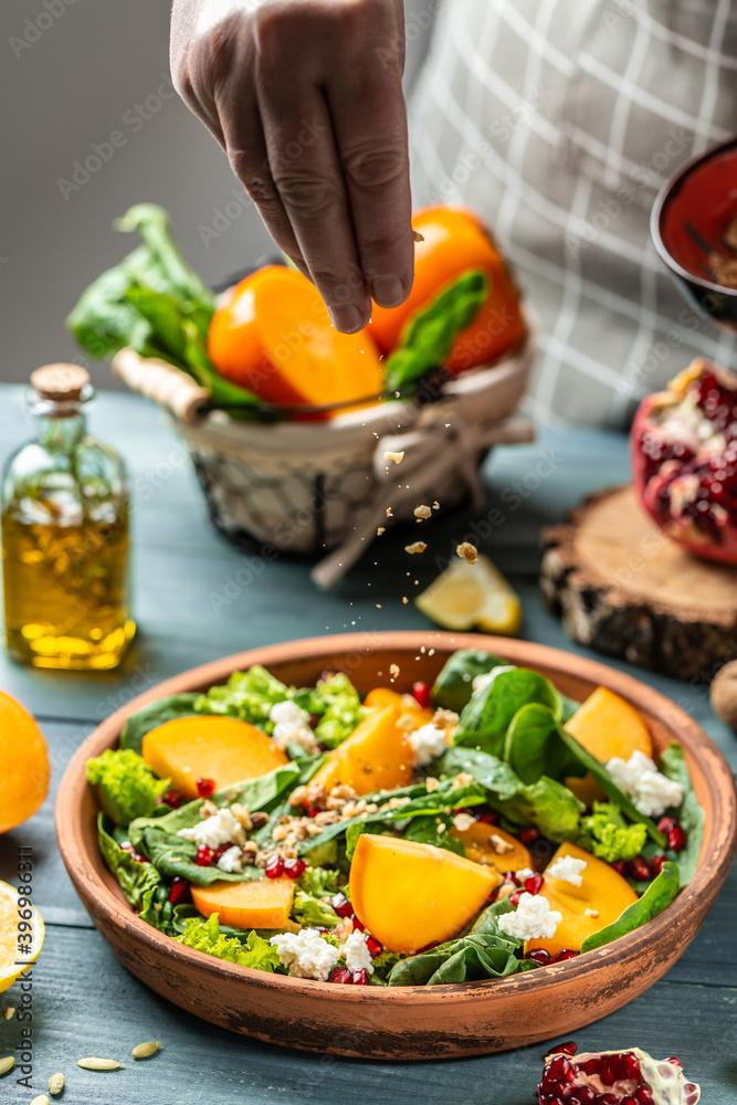Healthy salad with persimmons, spinach, nuts, goat cheese, pomegranate and pumpkin seeds. Freezer food prepare in process vegetarian salad by chef hand in home kitchen Healthy salad with persimmons, spinach, nuts, goat cheese, pomegranate and pumpkin seeds. Freezer food prepare in process vegetarian salad by chef hand in home kitchen