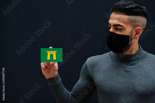 Egyptian man in gray turtleneck and black face protect mask show Qena flag isolated background. Governorates of Egypt coronavirus concept. photo