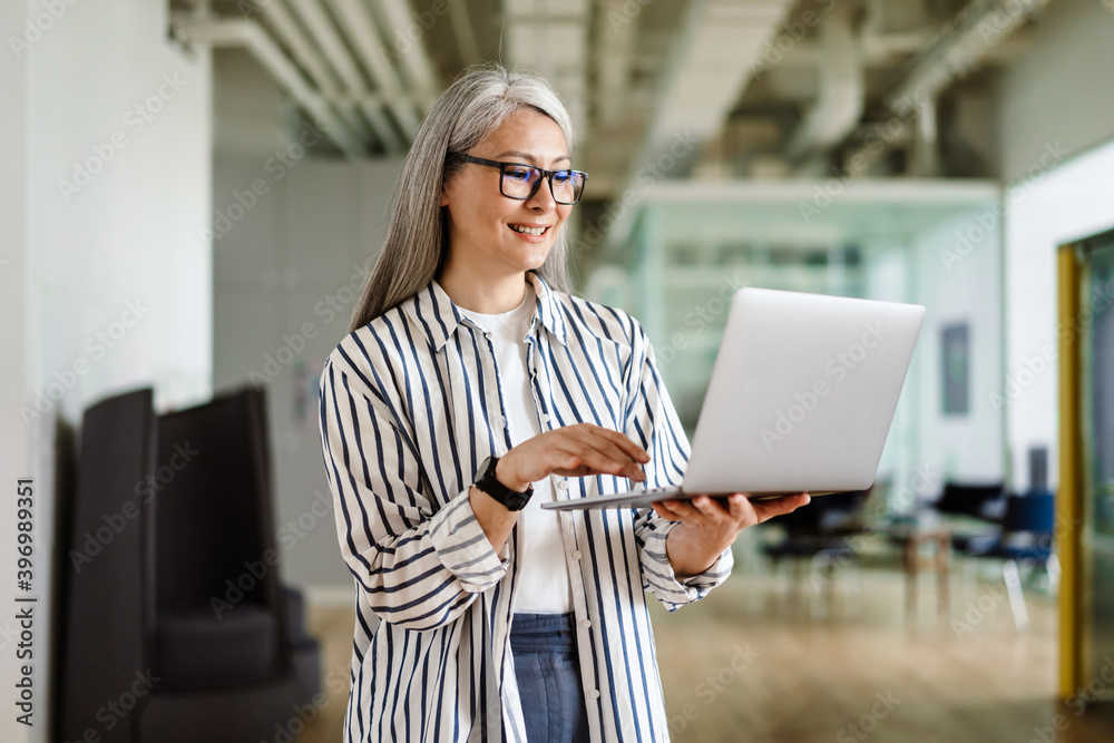 Happy white-haired mature woman smiling while using laptop Happy white-haired mature woman smiling while using laptop