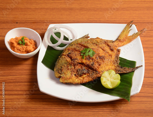 Pomfret fish tawa fry garnished with lemon and onion in a white ceramic plate with wooden background,selective focus photo