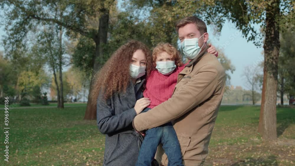 Young family in protective masks looking at camera in park, spread of virus Young family in protective masks looking at camera in park, spread of virus