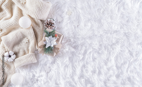 Winter cozy background with cup of coffee, warm sweater, gift box, cotton flower and christmas ball on wool carpet background, Top view with copy space.