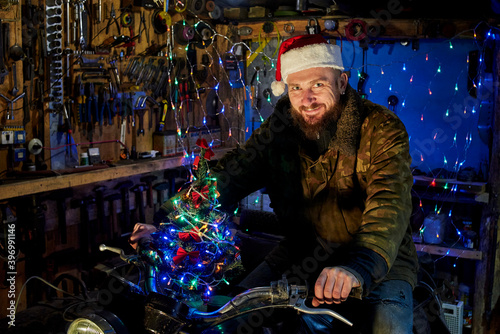 A man in a santa claus hat sitting on a motorcycle in the garage on New Year's Eve.