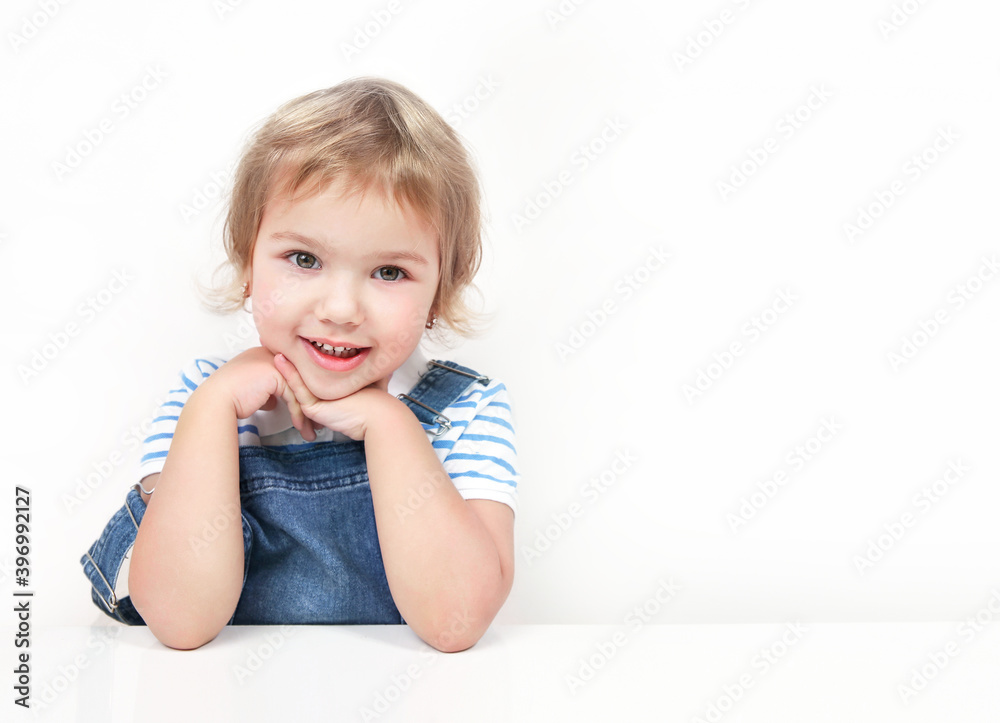 Caucasian child girl sitting at white empty table and smiling.Happy kid advertisement copy space. Caucasian child girl sitting at white empty table and smiling.Happy kid advertisement copy space.