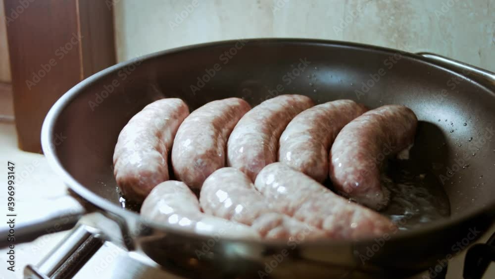 Closeup of cooking sausages in black pan with oil. Frying sausages in