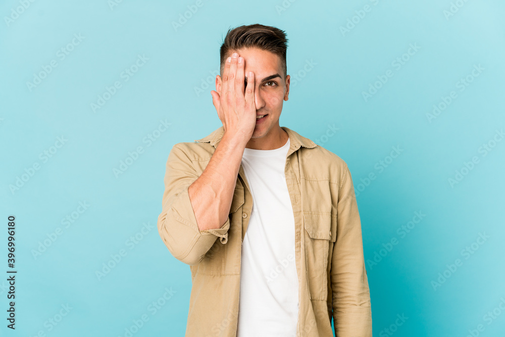 Young caucasian handsome man isolated having fun covering half of face with palm.