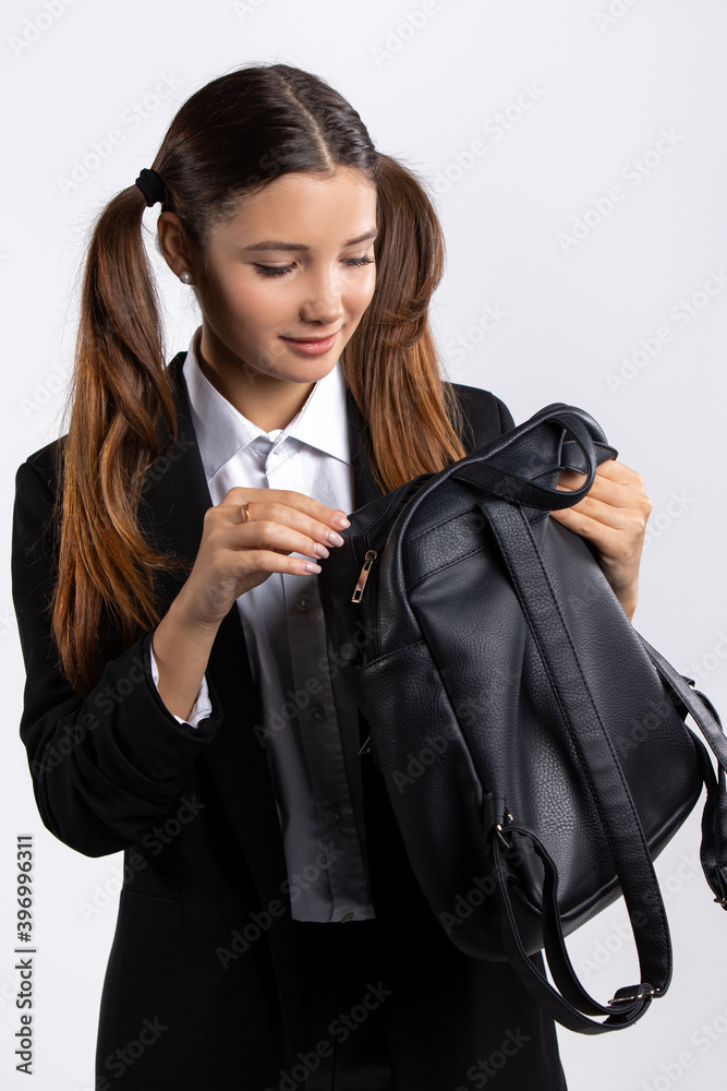 Schoolgirl in uniform opens her black bag. Portrait against white background. Schoolgirl in uniform opens her black bag. Portrait against white background.