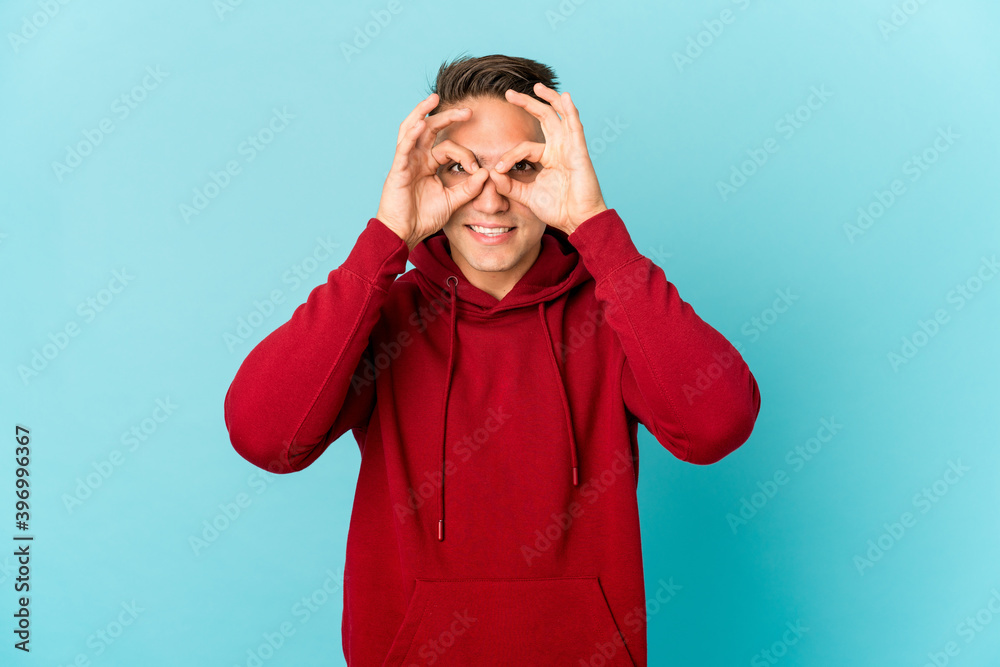 Young caucasian handsome man isolated showing okay sign over eyes Young caucasian handsome man isolated showing okay sign over eyes
